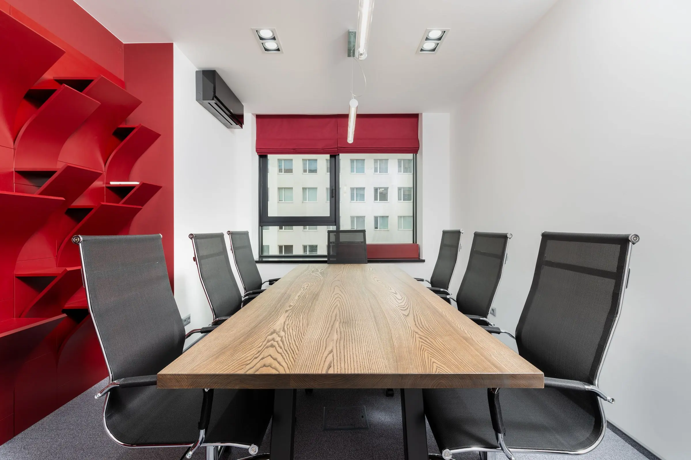 Sala de reuniones con mesa de madera y pared roja junto a la ventana