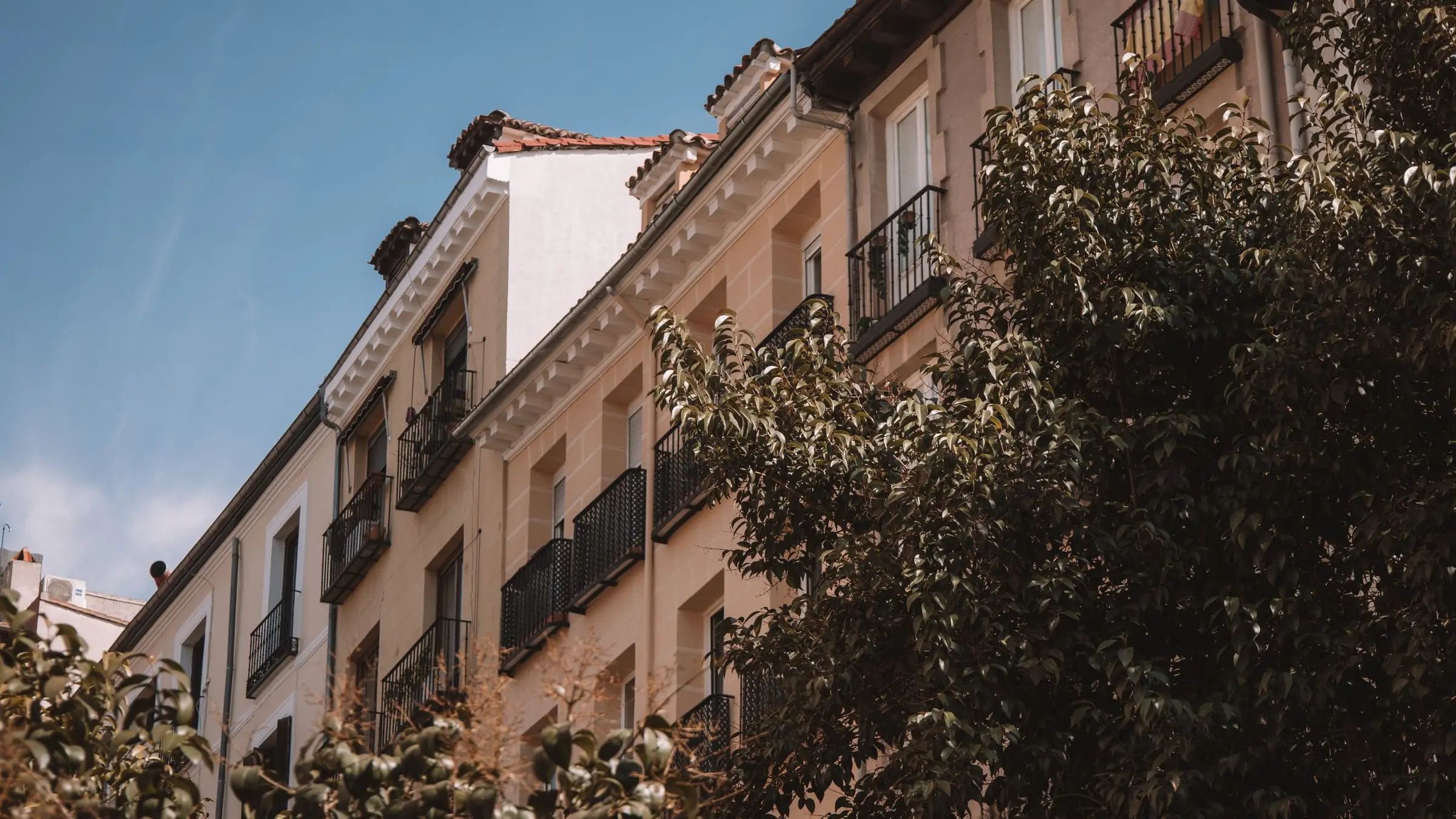 Fachada de un edificio de viviendas con balcones de hierro en una calle arbolada
